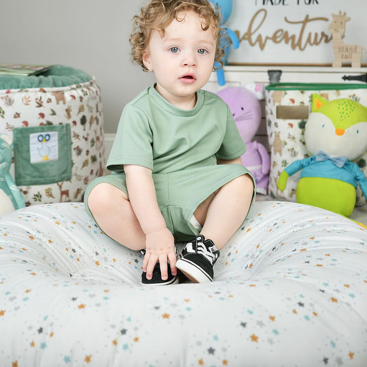 Young toddler sitting on Pello Lunar Floor Cushion that features a white background with colored stars.  