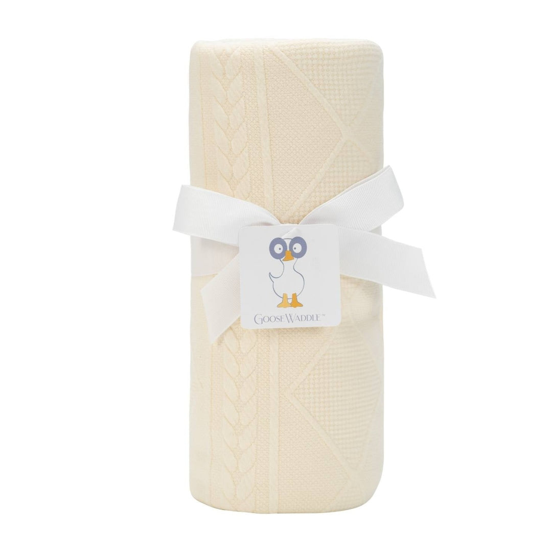 A oatmeal knit blanket rolled up with a white ribbon and tagged with a card featuring an owl.