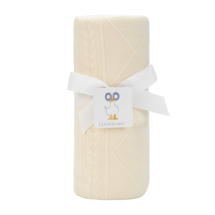 A oatmeal knit blanket rolled up with a white ribbon and tagged with a card featuring an owl.