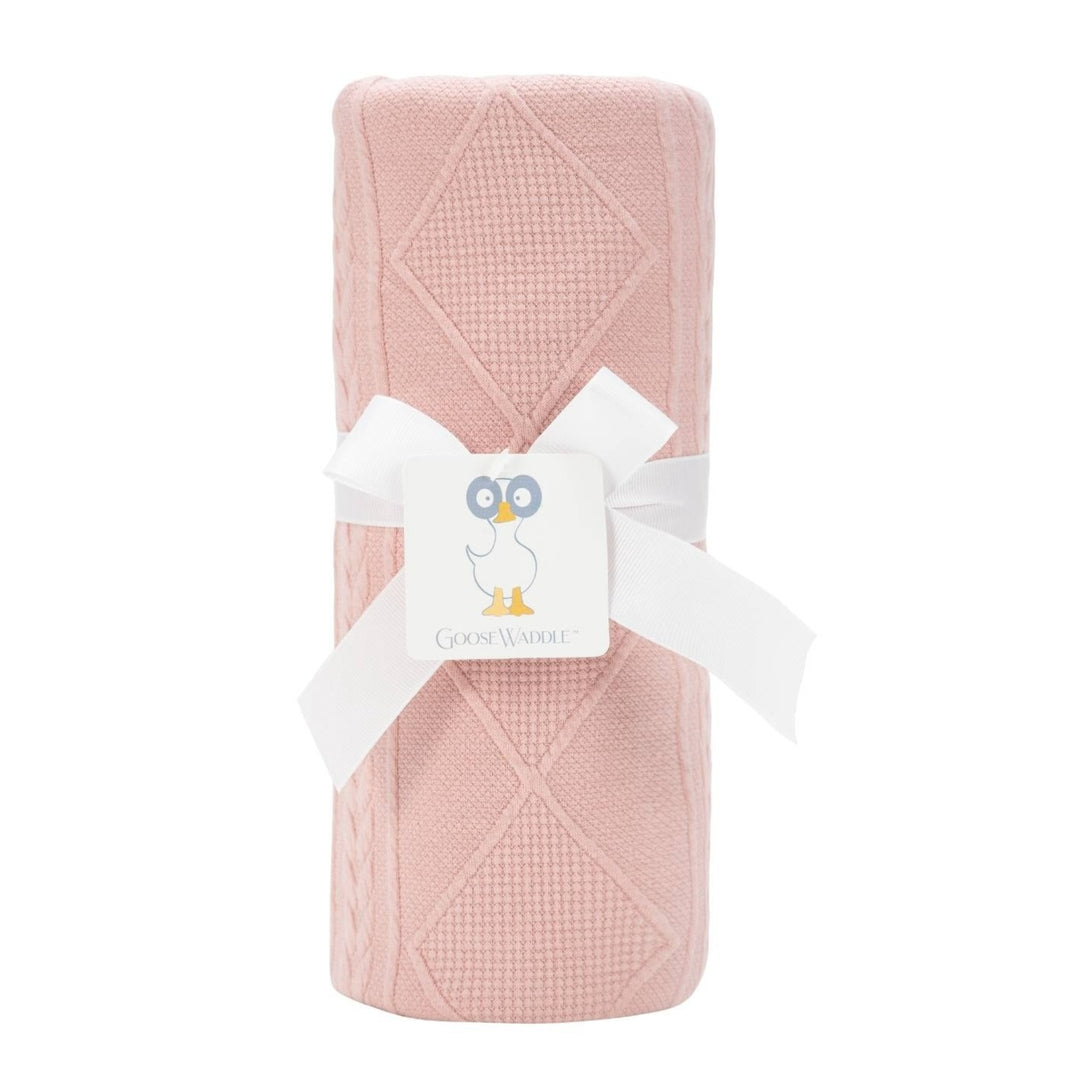 A pink rose colored knit blanket with a geometric pattern, wrapped with a white ribbon and tagged with a card showing a blue duck and the brand name.