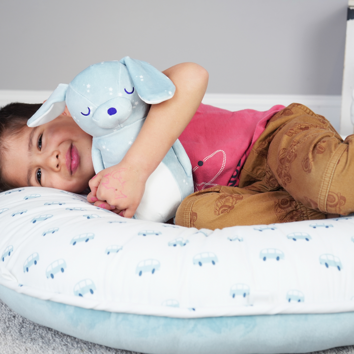 Tag (cars) Floor Cushion with a young boy resting in it and snuggling Atlas Puppy plush.