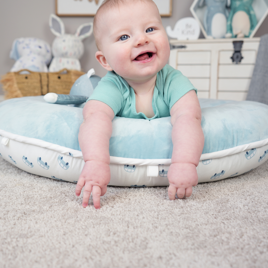 Young child laying across Tag Floor Cushion (white with blue cars) and smiling.